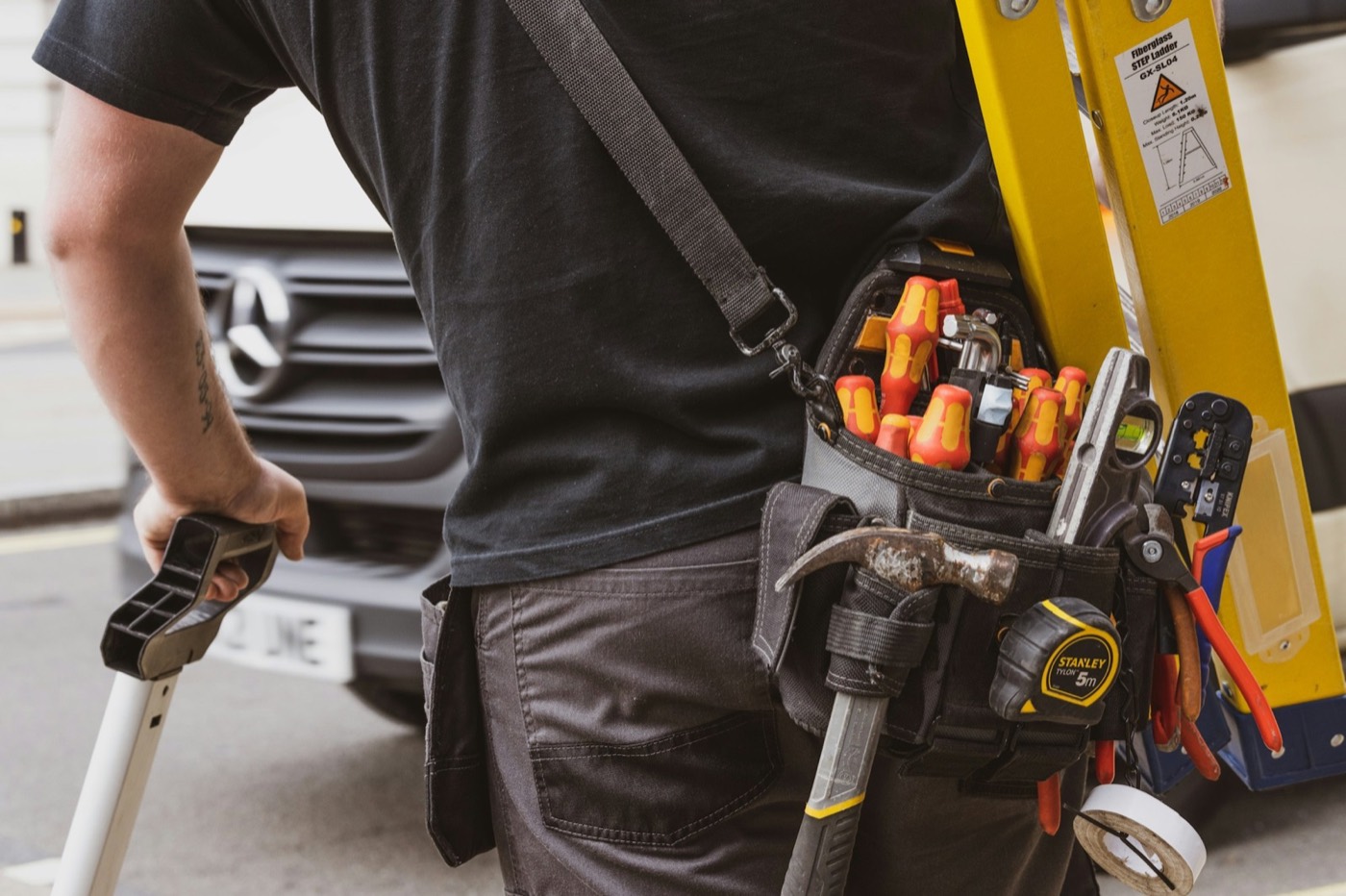 Contractor with a tool belt carrying a ladder
